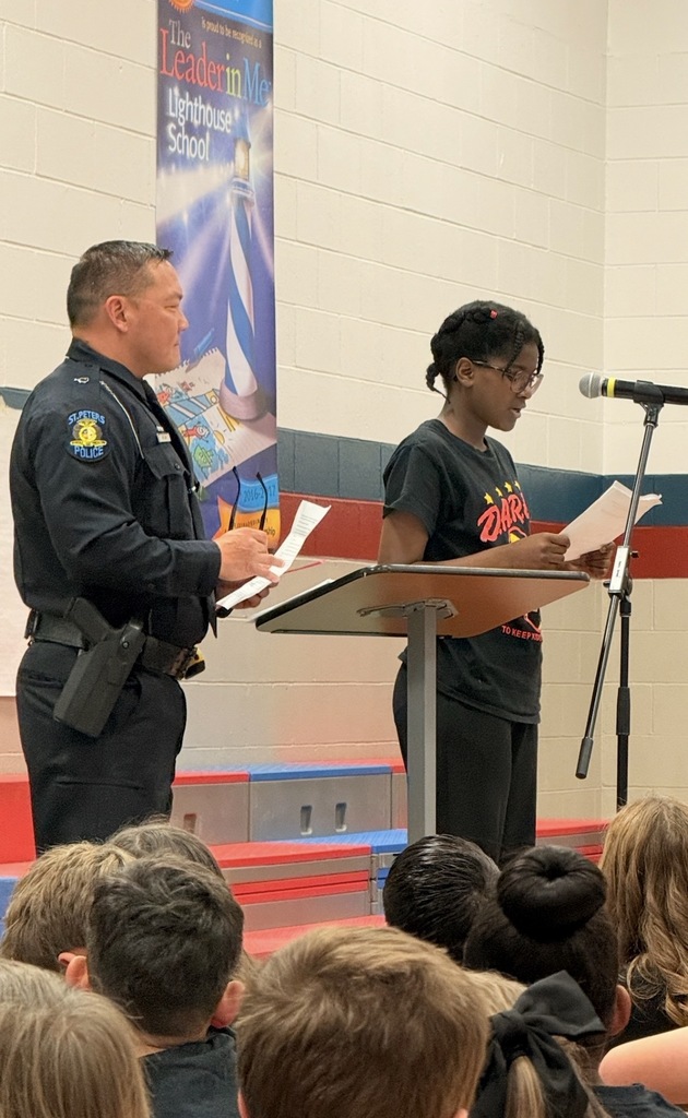 A 5th grade student reading her DARE essay with pride with Officer Luu standing behind her smiling proudly.