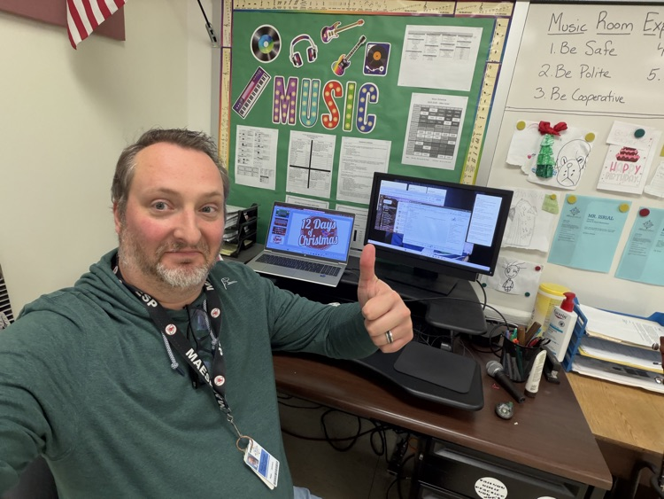 man in green hoodie giving a thumbs up. Man is sitting in front of a laptop and a monitor