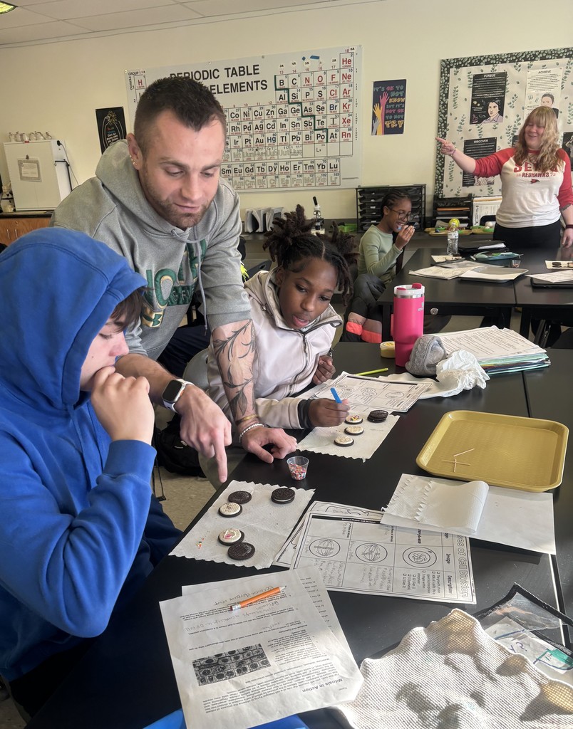 A teacher is helping two students use sprinkles and oreos to understand mitosis phases in class.