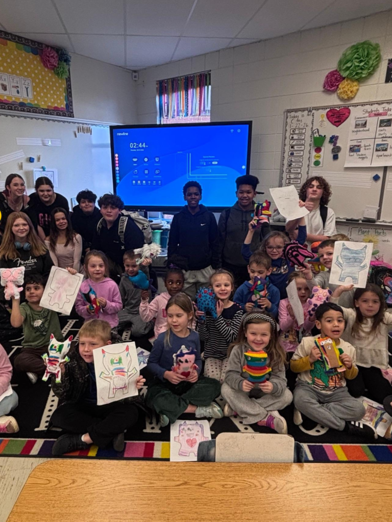 Kindergarteners pose with their illustrations, their monsters, and their 8th grade buddies