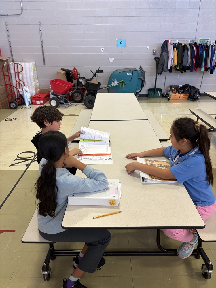three students sitting at tables sharing portfolios of work