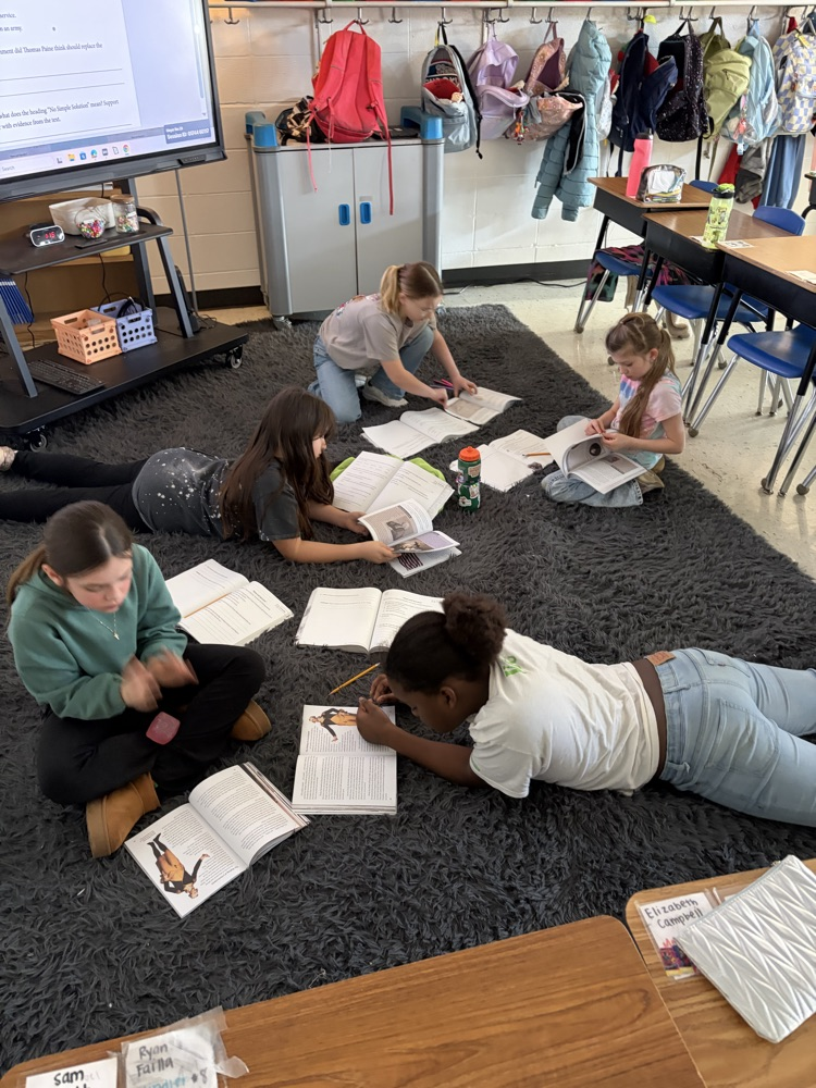 students sitting on a carpet reading and sharing ideas with one another