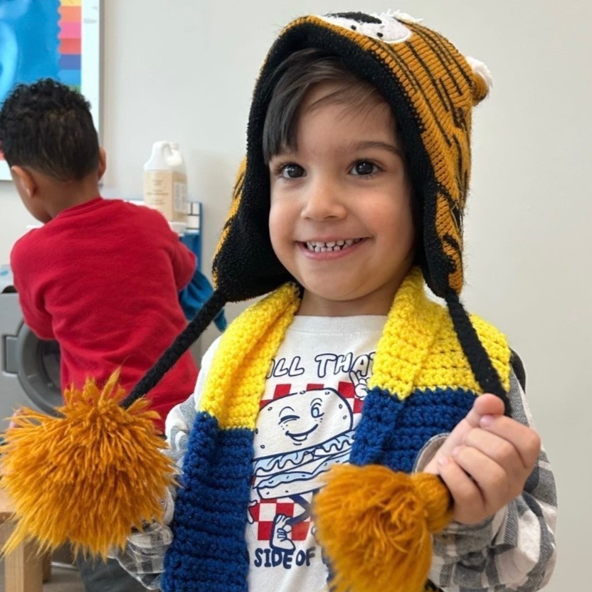 Pre K student smiles with pride after dressing for winter in hat and scarf