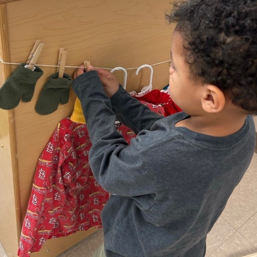 Pre-K student works fine motor and sorting skills hanging clothes on a clothes line