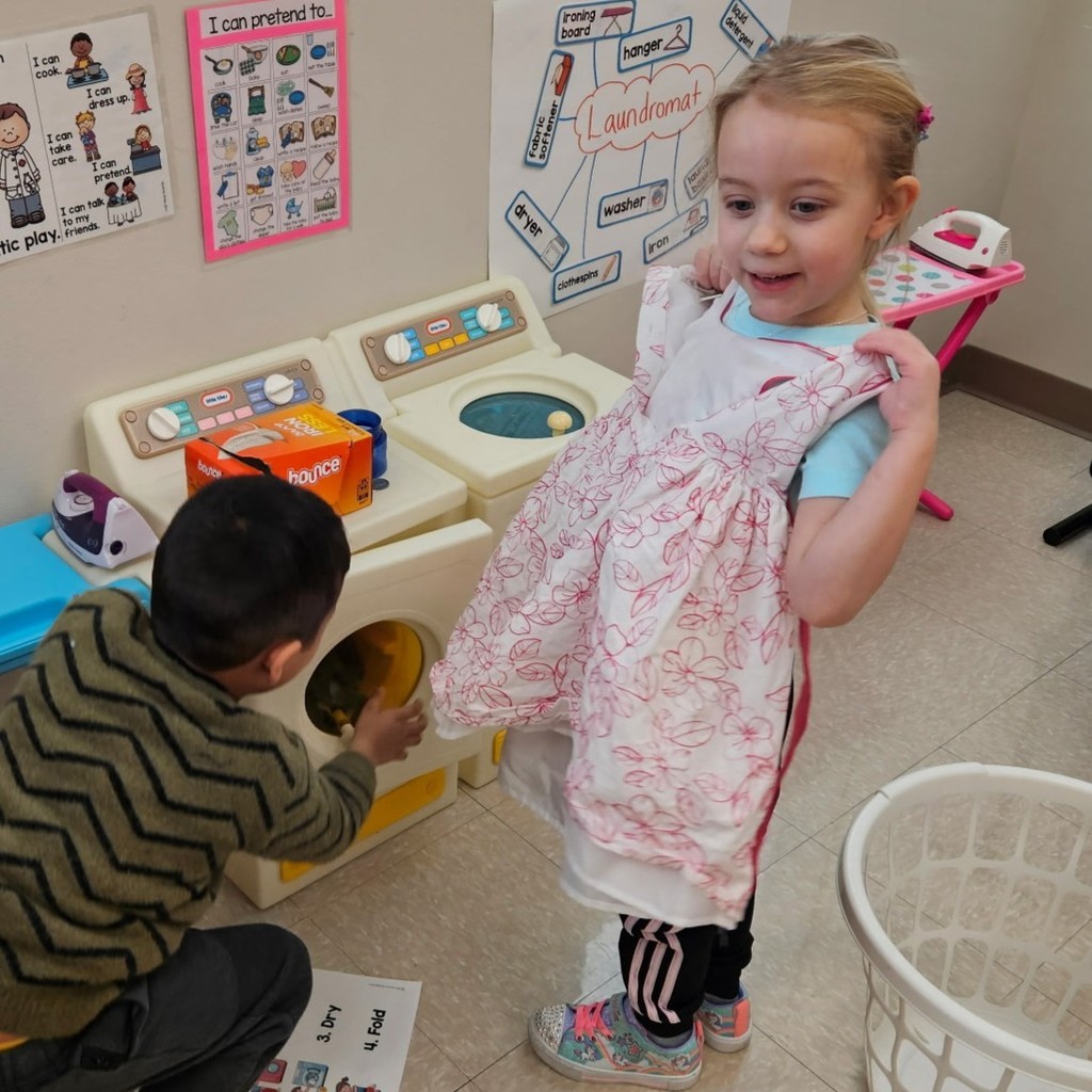 Pre K students take turns loading and unloading toy laundry machines