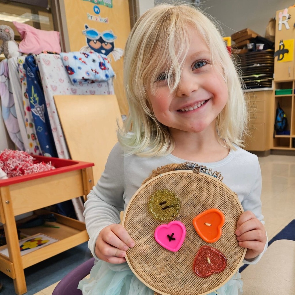 Pre K student shows off buttons threaded into burlap