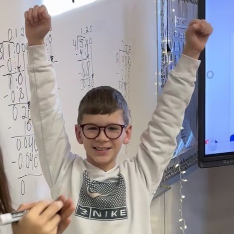 Success! Smiling student in glasses throws arms in the air to celebrate successfully solving a problem