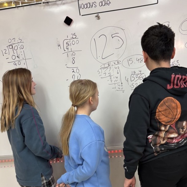 Students discuss their work, shown on a wipe board, and how they found different routes to the same solution