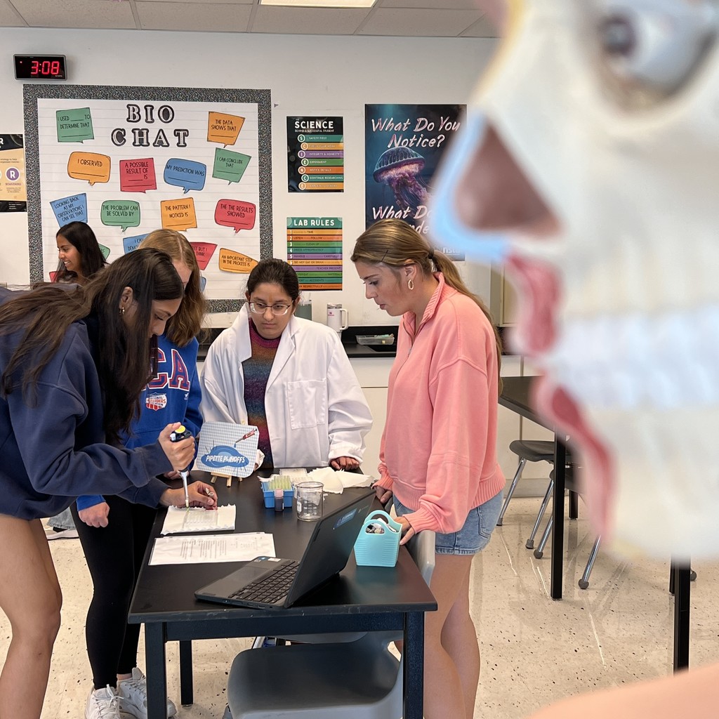 With plastic body systems model in foreground, students in white medical coat conduct experiement