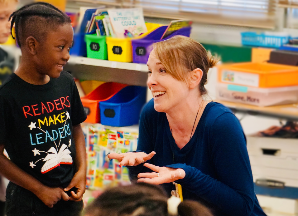 Kindergartener and teacher smile as they discuss book they are reading