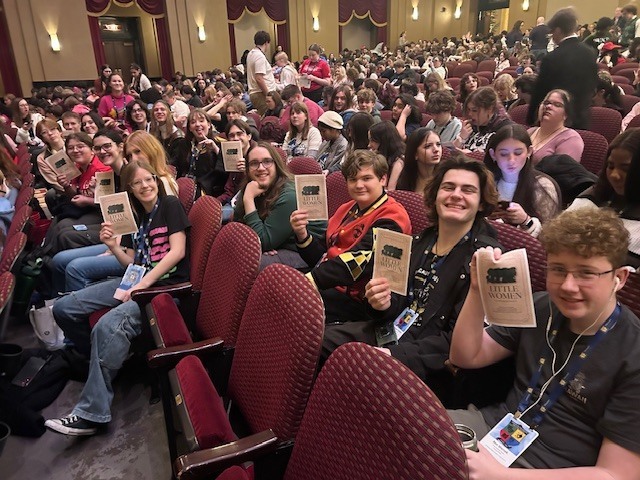 Students in theater seats smile and hold up Playbills before a show