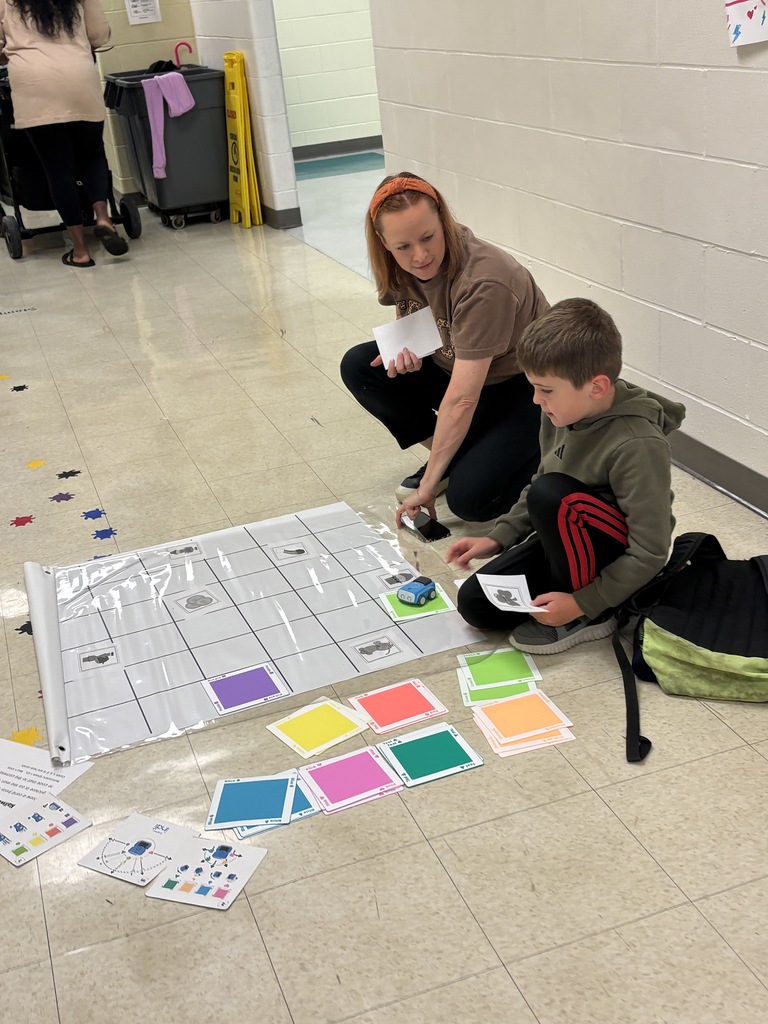 Mrs. Bedford helping a student figure out how to place mats on the chart to code his robot
