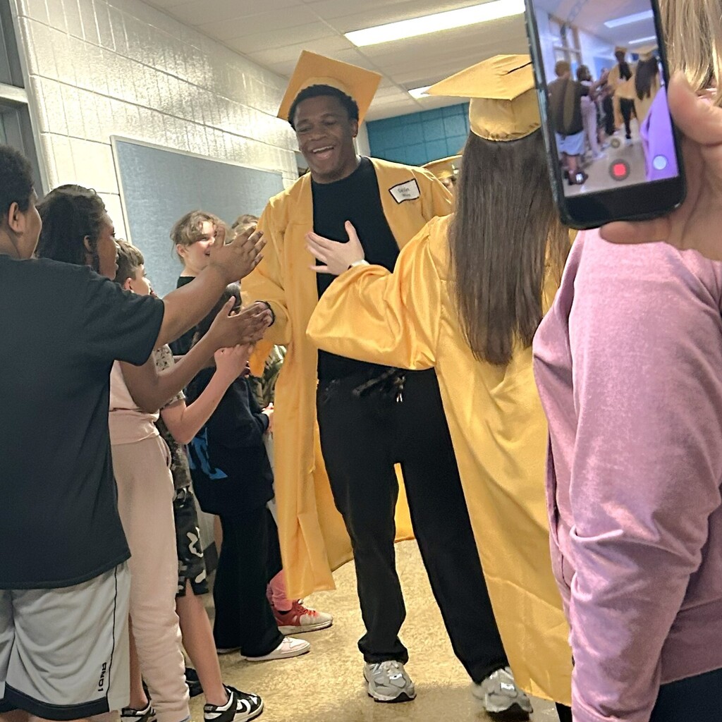grad in cap and gown high fives elementary school students