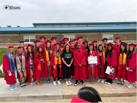 teacher poses with former students in their caps and gowns