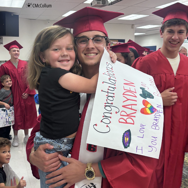grad in cap and gown with kindergartner homemade sign