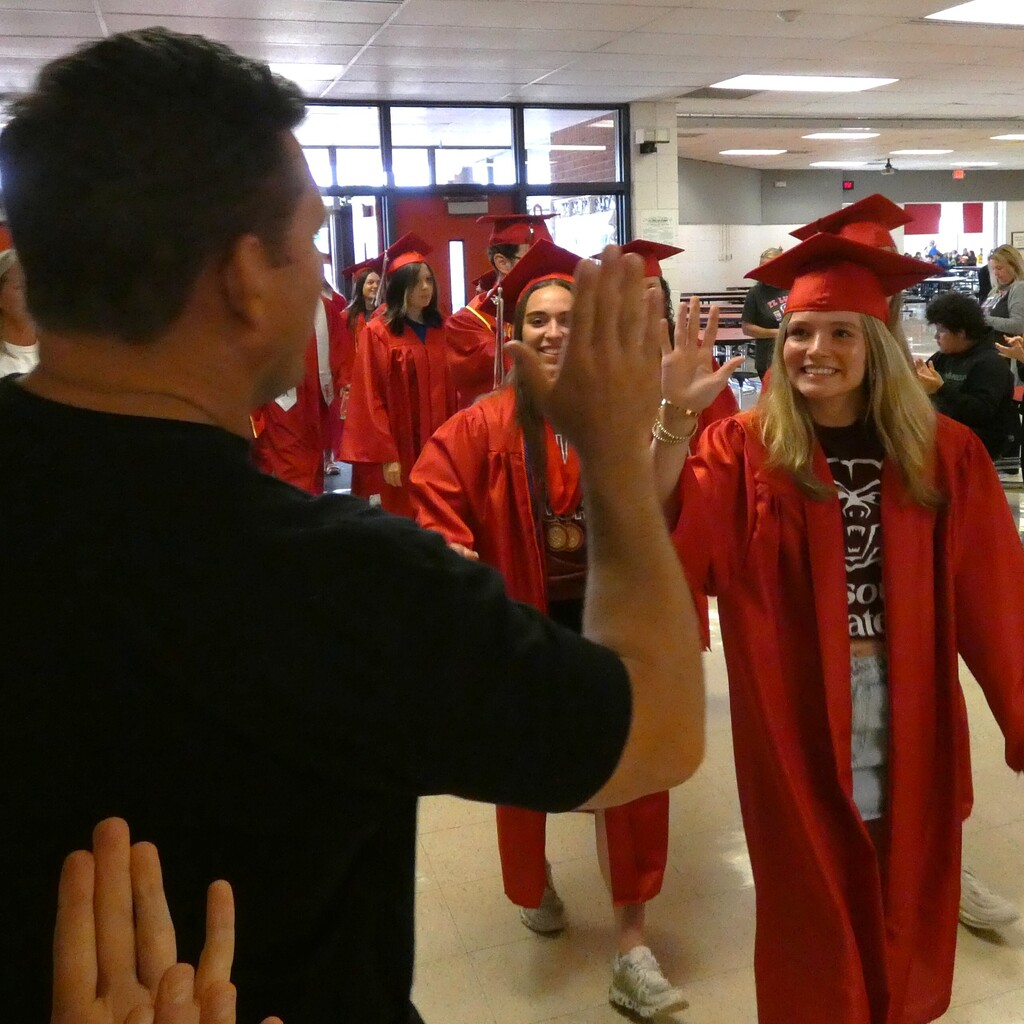 grad in cap and gown high fives former teacher