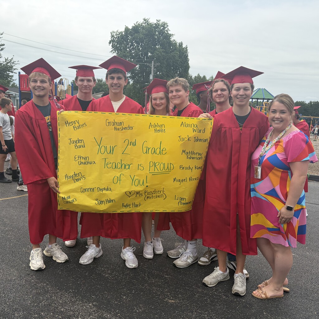 grads in caps and gown with former teacher and banner that says Your 2nd Grade Teacher is Proud of You