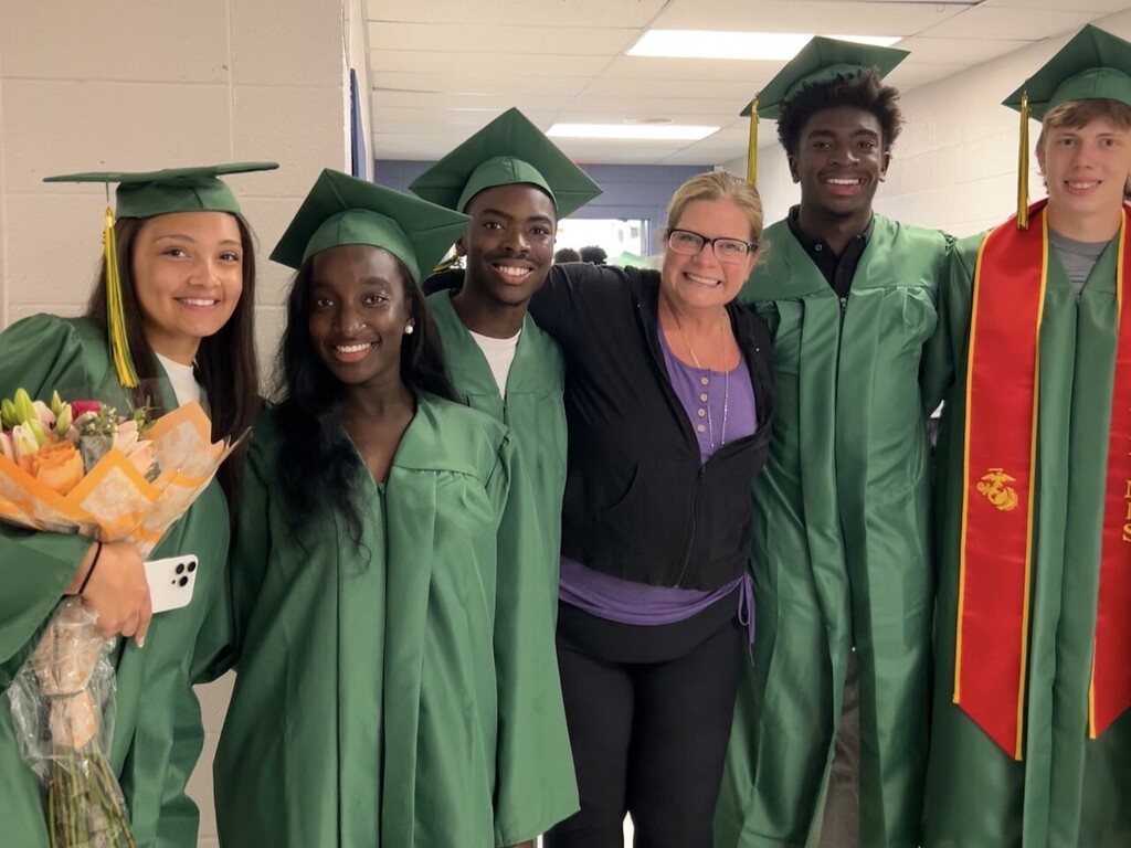 teacher flanked by former students in caps and gowns
