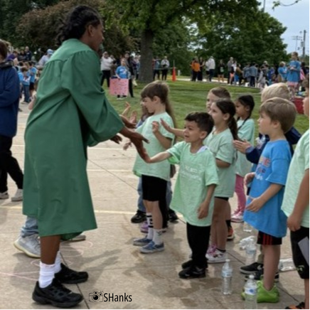 student in cap and gown high fives elementary students