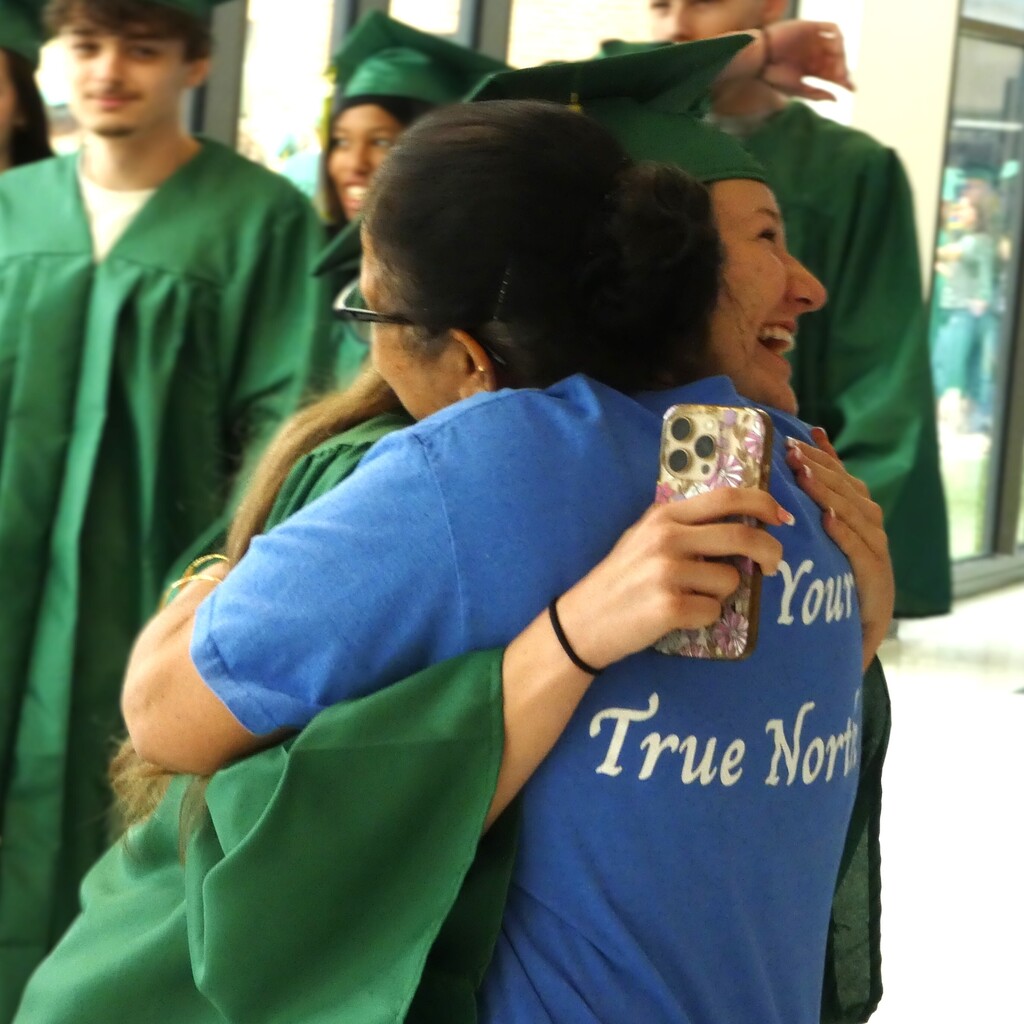 student in cap and gown hugs former teacher