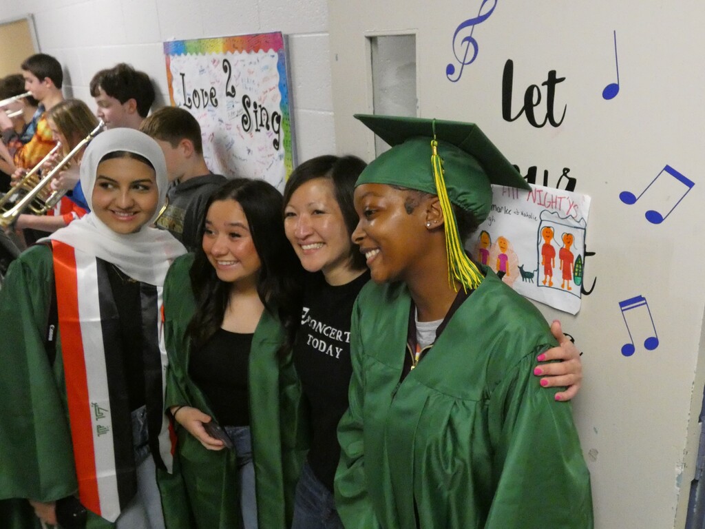 teacher flanked by former students in caps and gowns