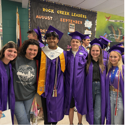 teacher flanked by former students in caps and gowns