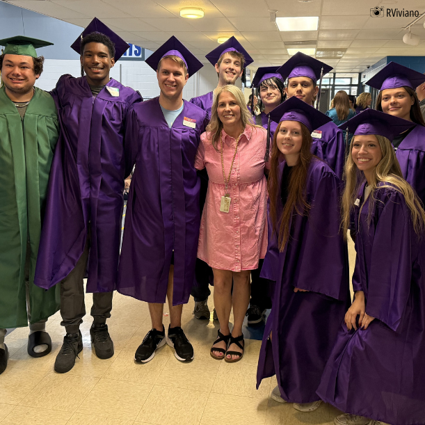 teacher flanked by former students in caps and gowns