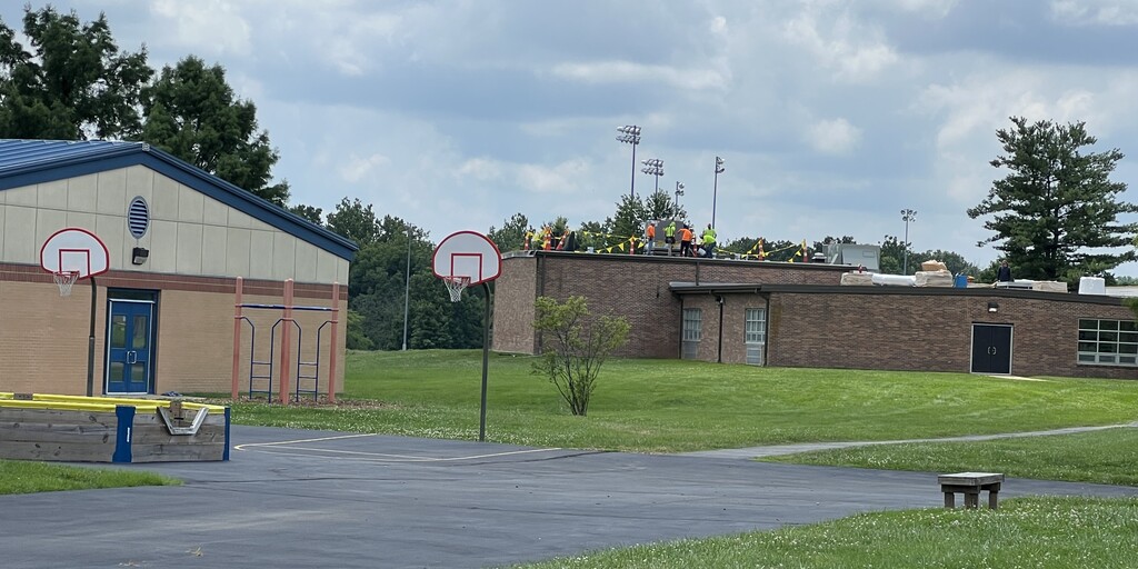 Workers in neon safety shirts on the school roof, bordered by warning flags