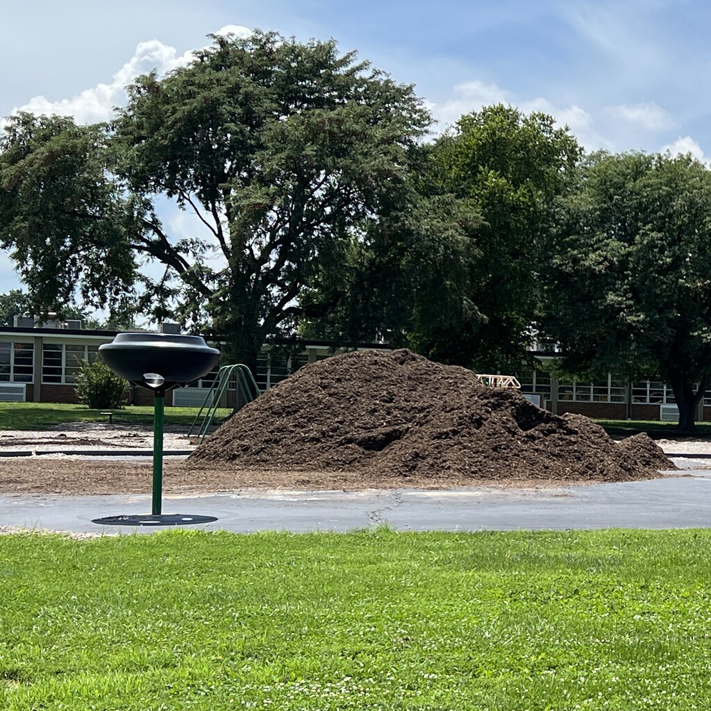 Mulch piled as high as the playground equipment before being spread across play area