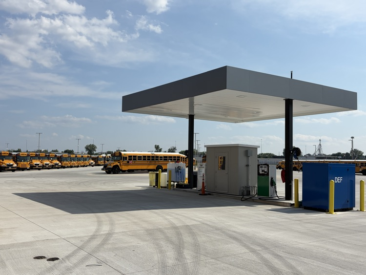 fueling station - a covered structure with a gas pump, dozens of school buses in the background