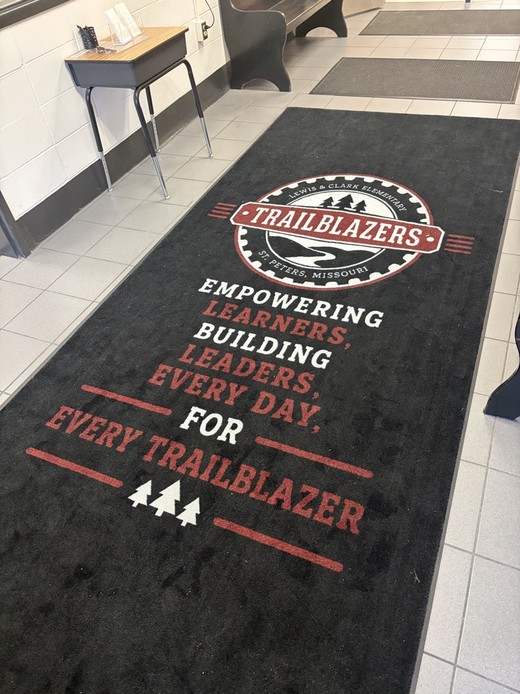 black rug, white and red lettering. reads “empowering leaders building learners - every day for every Trailblazer.”