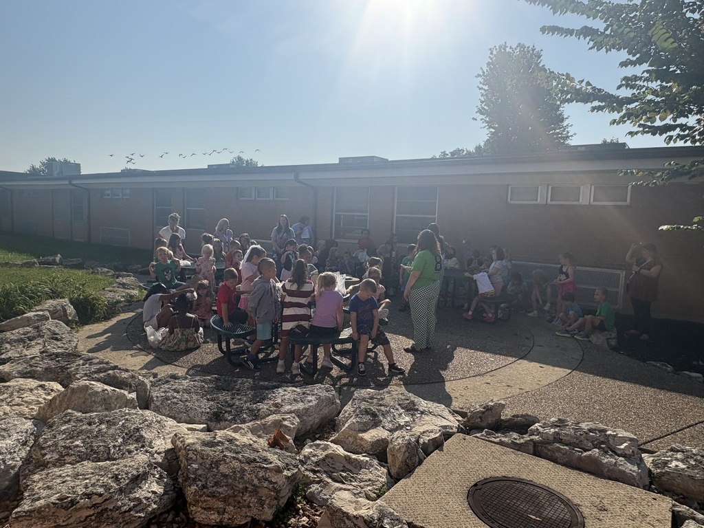 Adults with students in an outdoor classroom talking and looking at a pond.