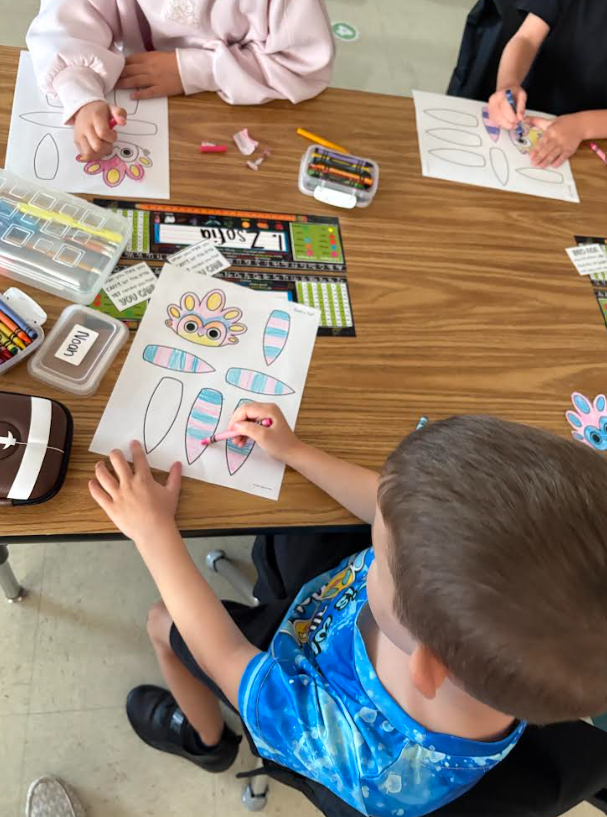 Three children at a desk coloring pictures.