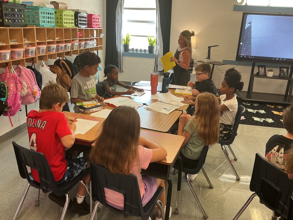 Several students are sitting at their desks listening to their teacher and taking notes.
