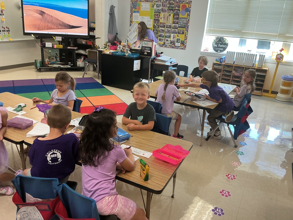 Several students are sitting at tables working on a coloring page.