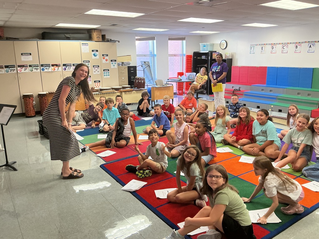 Teacher teaching students who are on a multi-colored rug with worksheets.