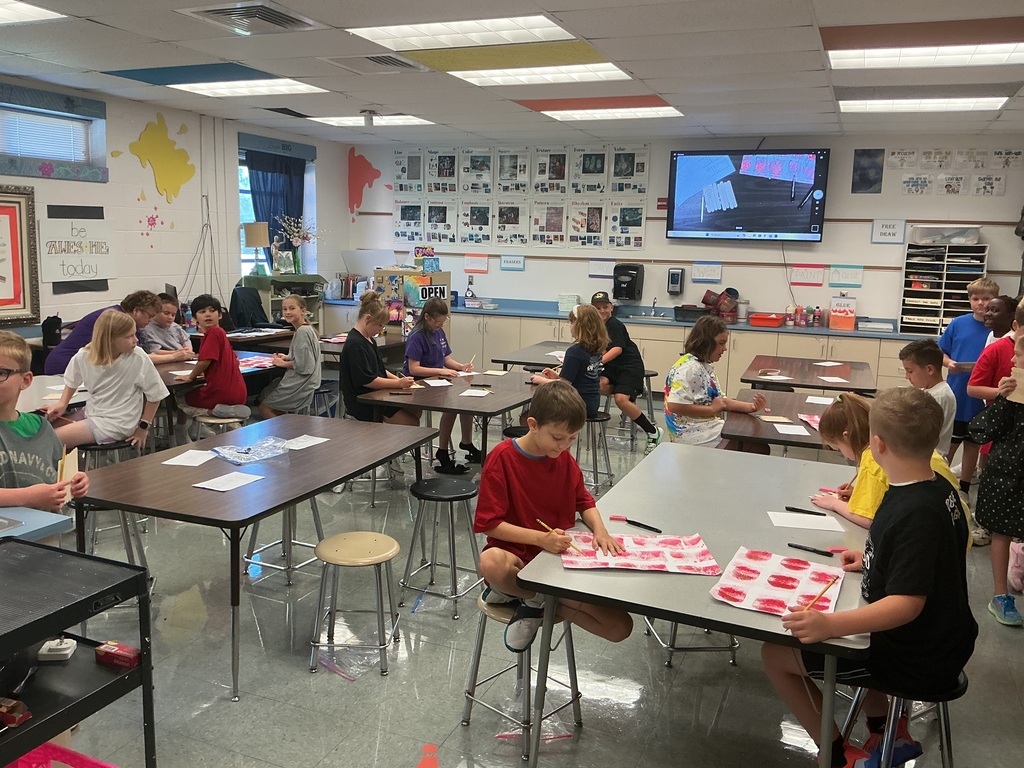 Students in an art classroom creating paintings with red paint.