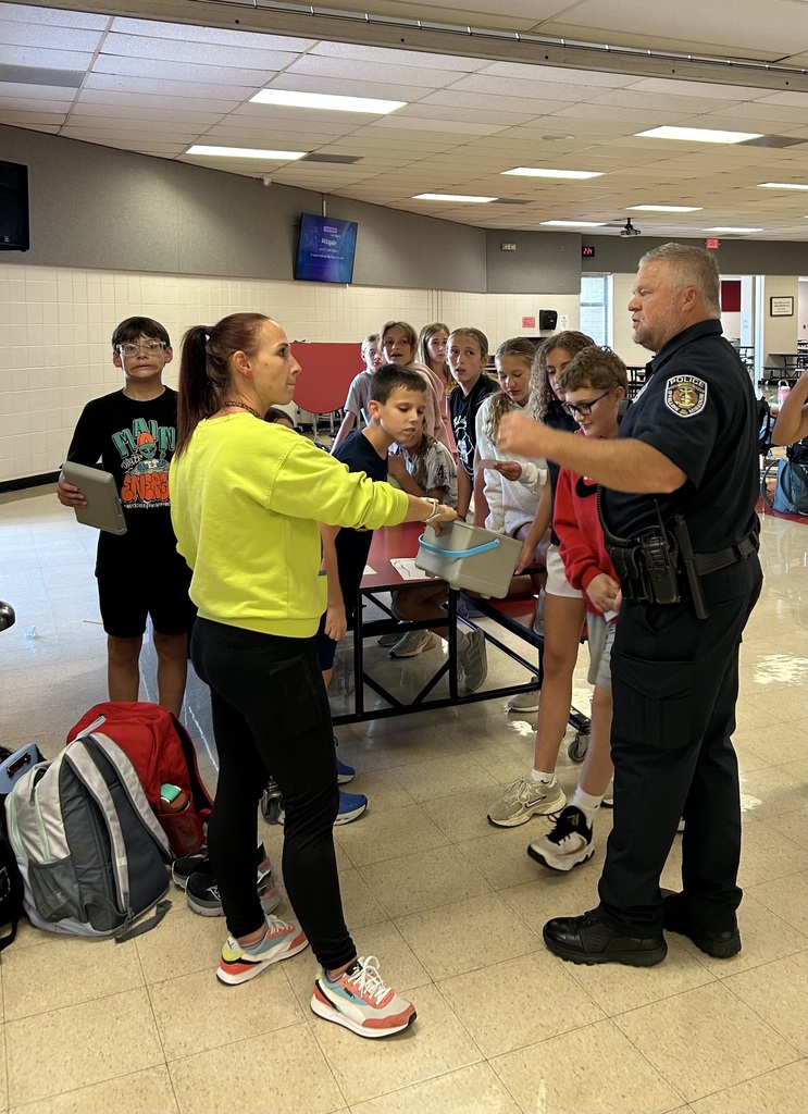 Officer Budds and students  listening to Mrs. Young share what’s next for the Running Club and their upcoming fun run activity!