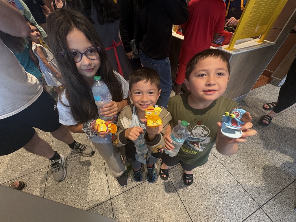 Three children holding up toys and water bottles at a restaurant.