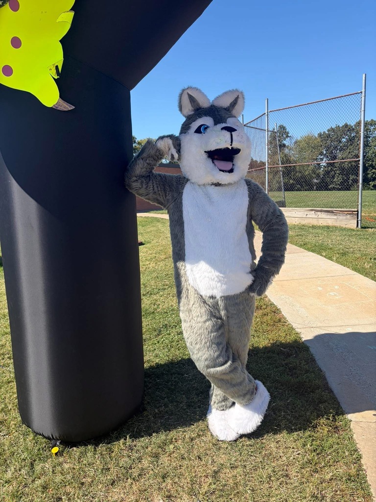 A husky dog mascot leaning on an inflatable pillar outdoors.