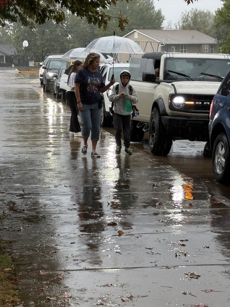 Students and teachers helping each other get to the school doors during rain.