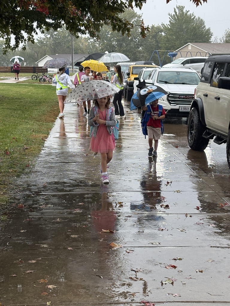 Students and teachers helping each other get to the school doors during rain.