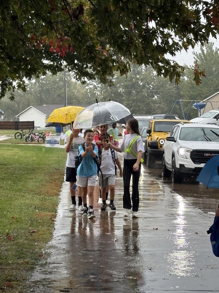 Students and teachers helping each other get to the school doors during rain.