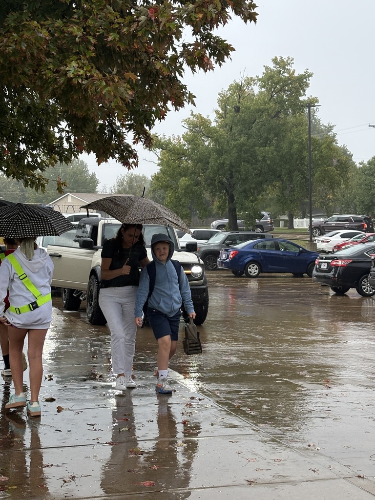 Students and teachers helping each other get to the school doors during rain.