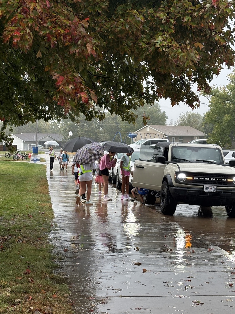 Students and teachers helping each other get to the school doors during rain.