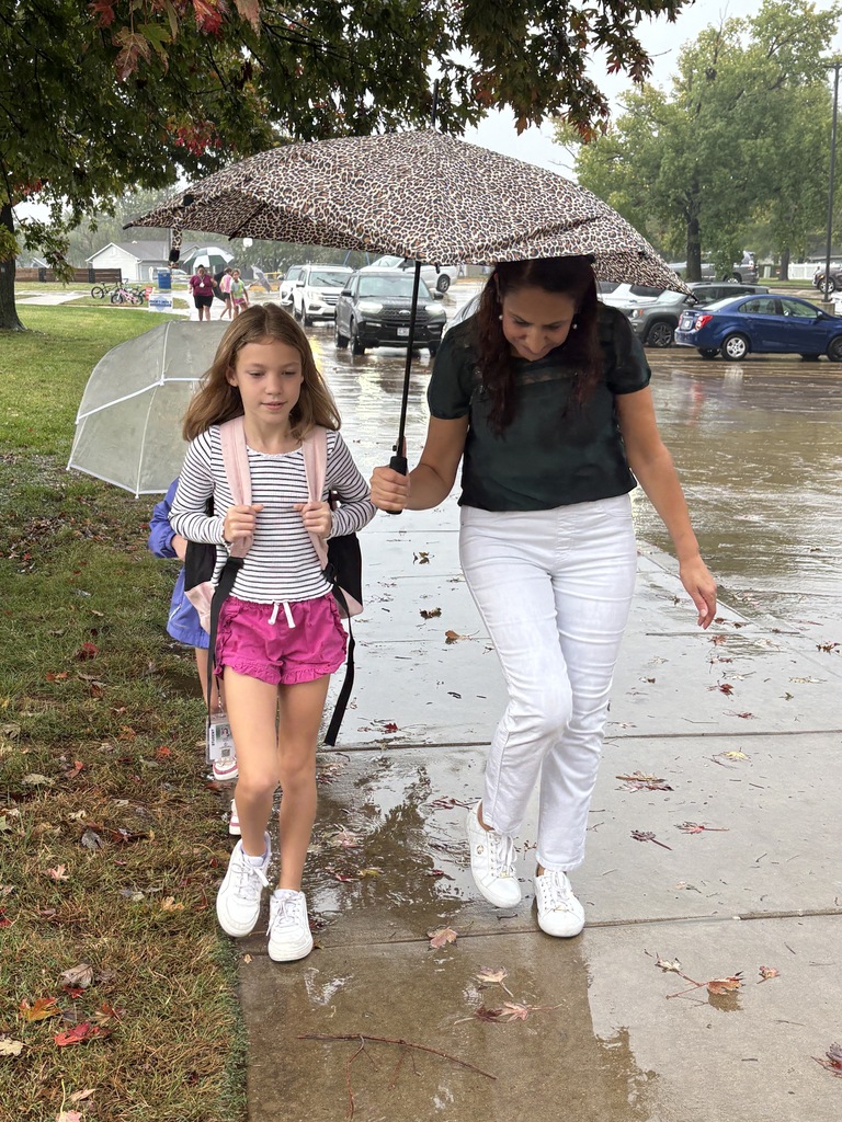 Students and teachers helping each other get to the school doors during rain.