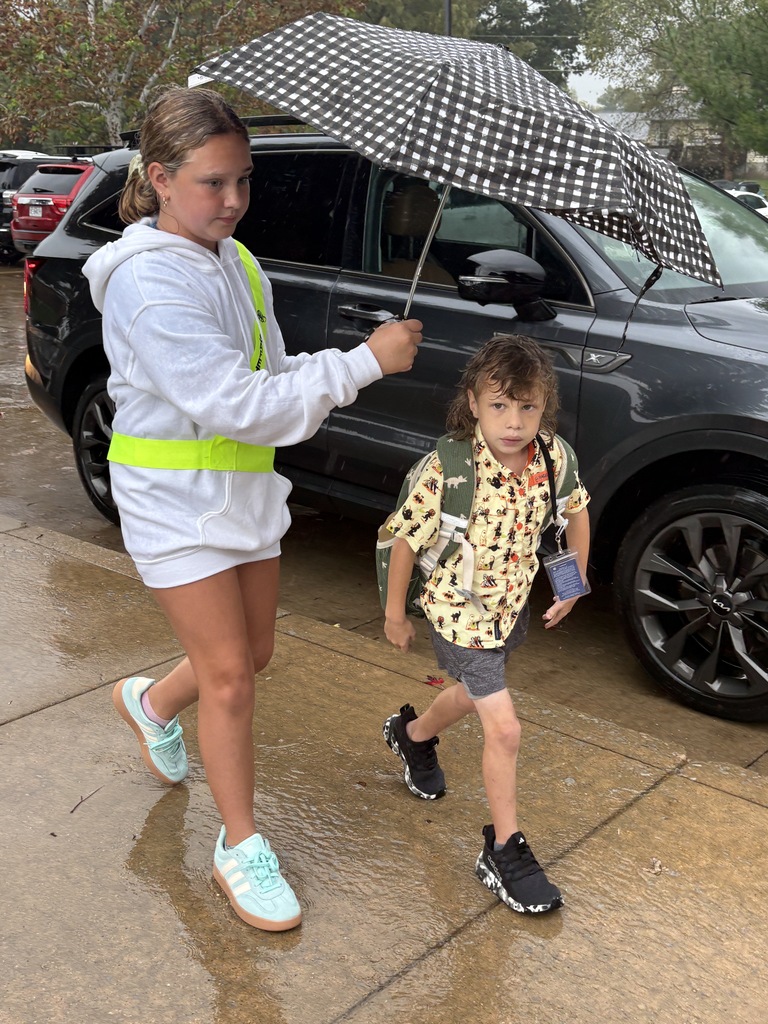 Students and teachers helping each other get to the school doors during rain.