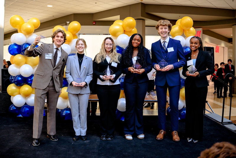 Erin Schimanski holding her trophy on stage with other competitors