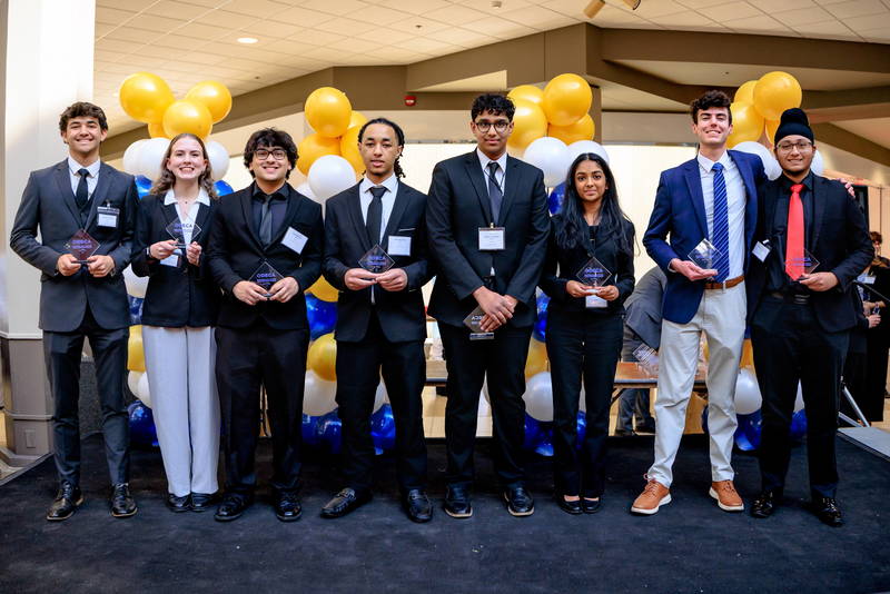 Theresa Strebeck and Cameron Jiang holding their trophies with other schools on stage