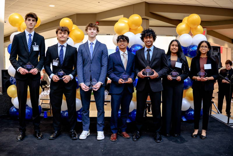 Owen Podmore and Luke Skinner holding their trophies with other schools on stage